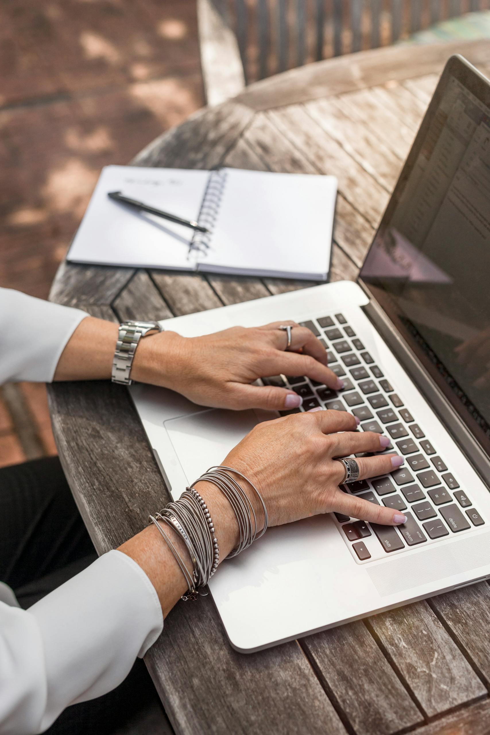 Hands typing on a laptop at an outdoor wooden desk, symbolizing remote work.