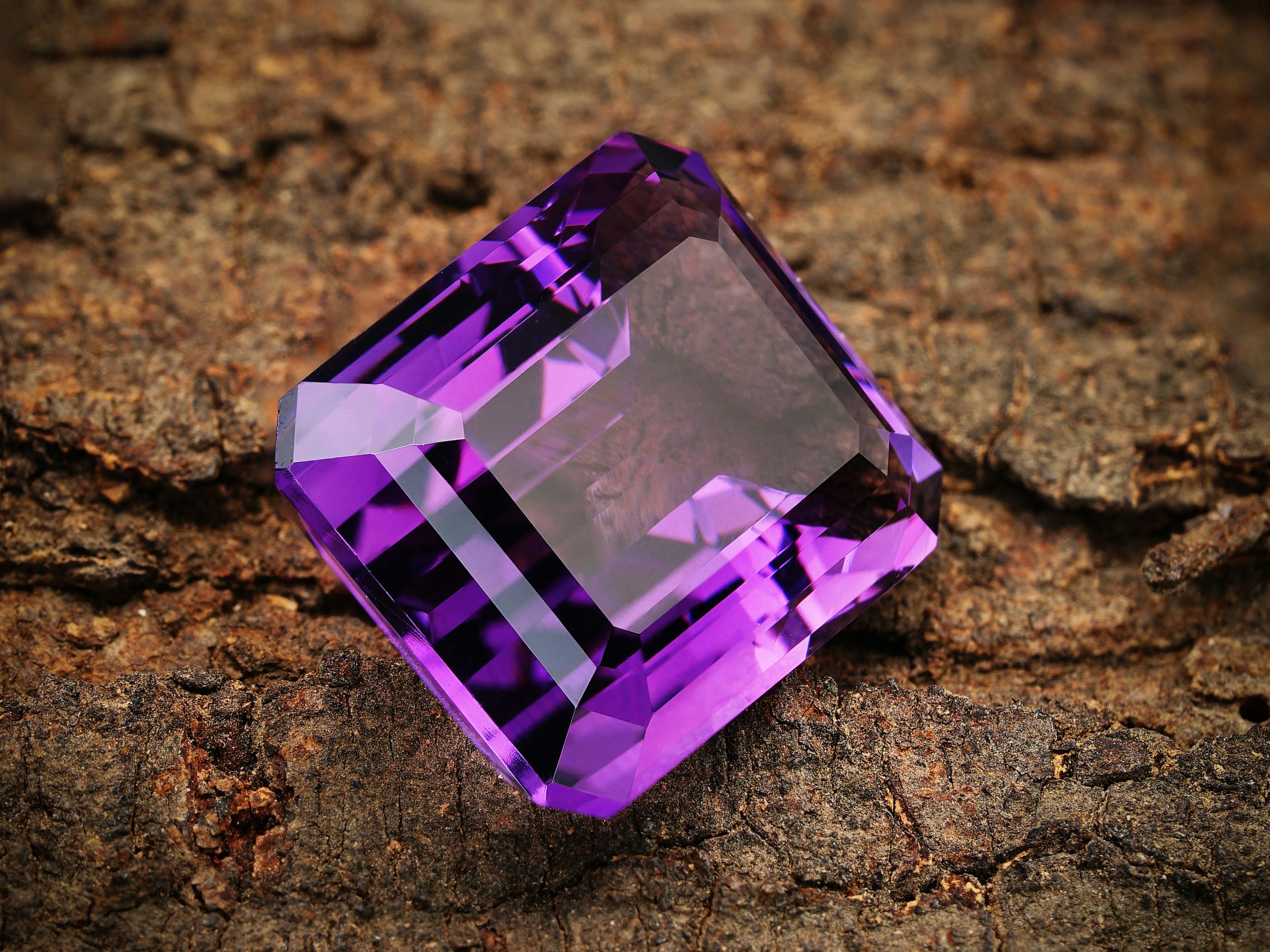 Close-up of a vibrant purple amethyst gemstone resting on a textured brown background.